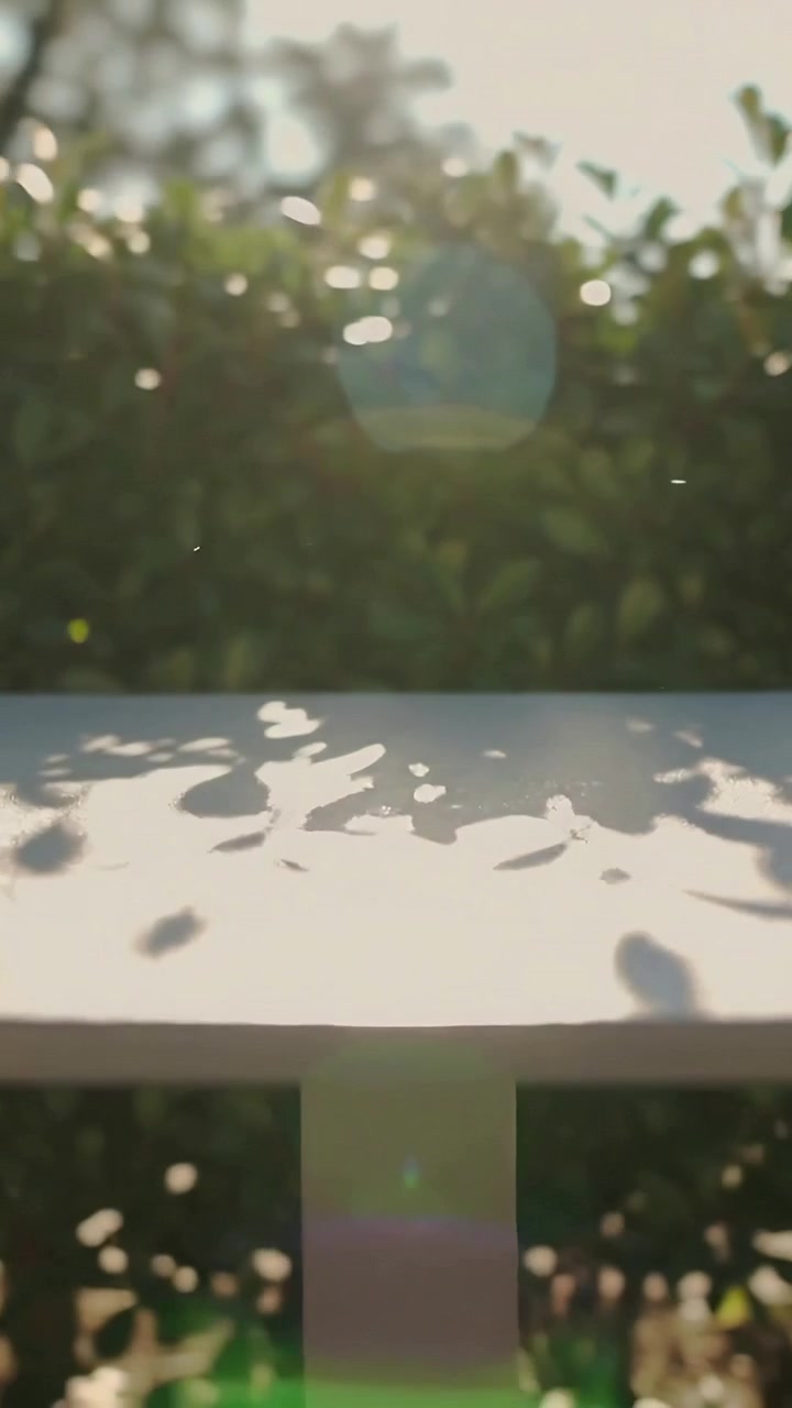 Vertical video: Sunlight entering, camera tilting, revealing patio table casting shadows near hedge
