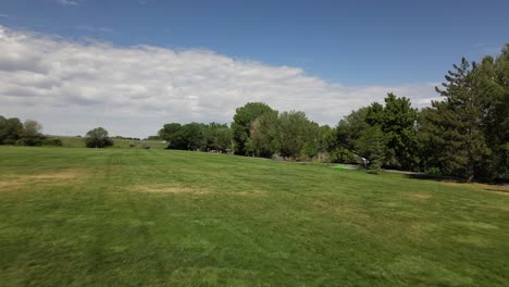 Kite-being-flown-by-little-boy-kid-child-at-large-green-open-field-park-as-drone-flies-quickly-to-the-left-of-him-on-beautiful-blue-sky-summer-day---in-4K-half-speed-30fps