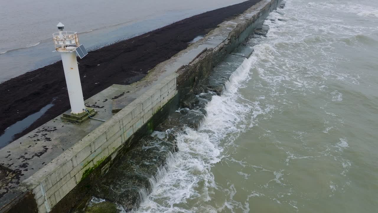 Aerial establishing view of Port of Liepaja concrete pier, Baltic sea coastline , foggy day with dense mist, moody feeling, big storm waves splashing, birdseye drone shot moving forward