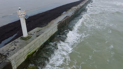 Aerial-establishing-view-of-Port-of-Liepaja-concrete-pier,-Baltic-sea-coastline-,-foggy-day-with-dense-mist,-moody-feeling,-big-storm-waves-splashing,-birdseye-drone-shot-moving-forward