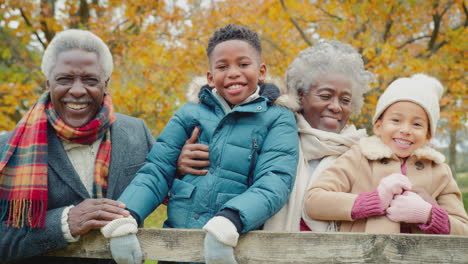 Porträt-Von-Großeltern-Mit-Enkelkindern,-Die-Sich-Bei-Einem-Gemeinsamen-Spaziergang-Durch-Die-Herbstliche-Landschaft-An-Ein-Tor-Lehnen-–-Aufgenommen-In-Zeitlupe