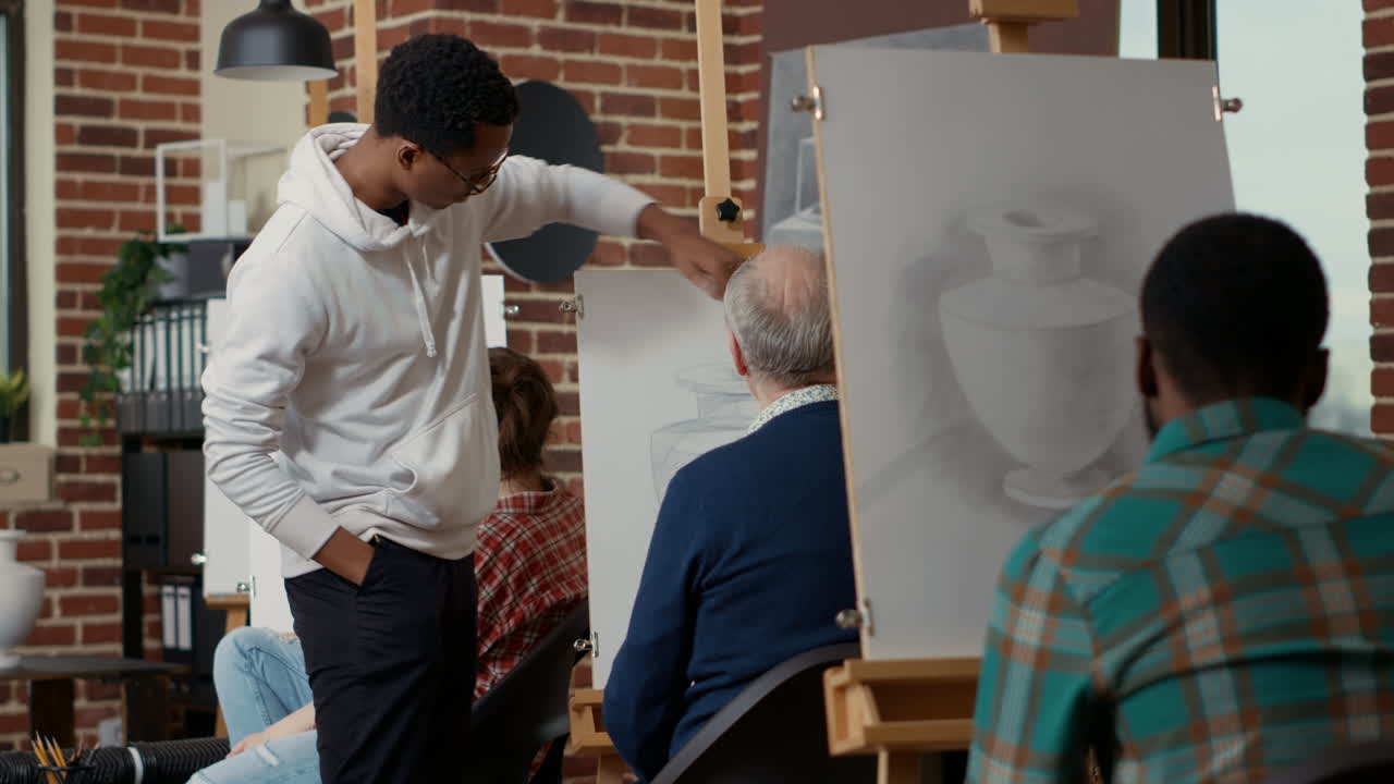 Young man looking at elder student drawing vase model