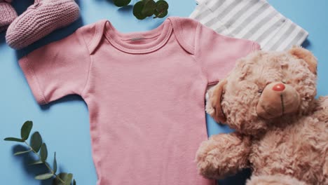 video of pink baby grow, booties, teddy bear and hat with copy space on blue background