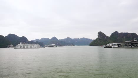 tourist cruise ships float serenely against the backdrop of ha long bay's iconic limestone karsts rising dramatically from emerald waters under an overcast sky in vietnam's most scenic seascape