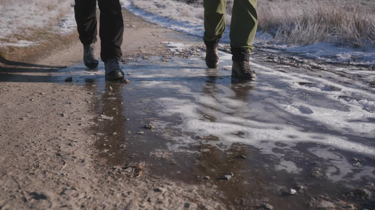 눈 덮인 황무지를 통과하는 겨울 길에서 하이킹을 하는 두 사람, 단단한 얼어붙은 얼음과 단단하게 포장된 흙 위를 걷고 있습니다.