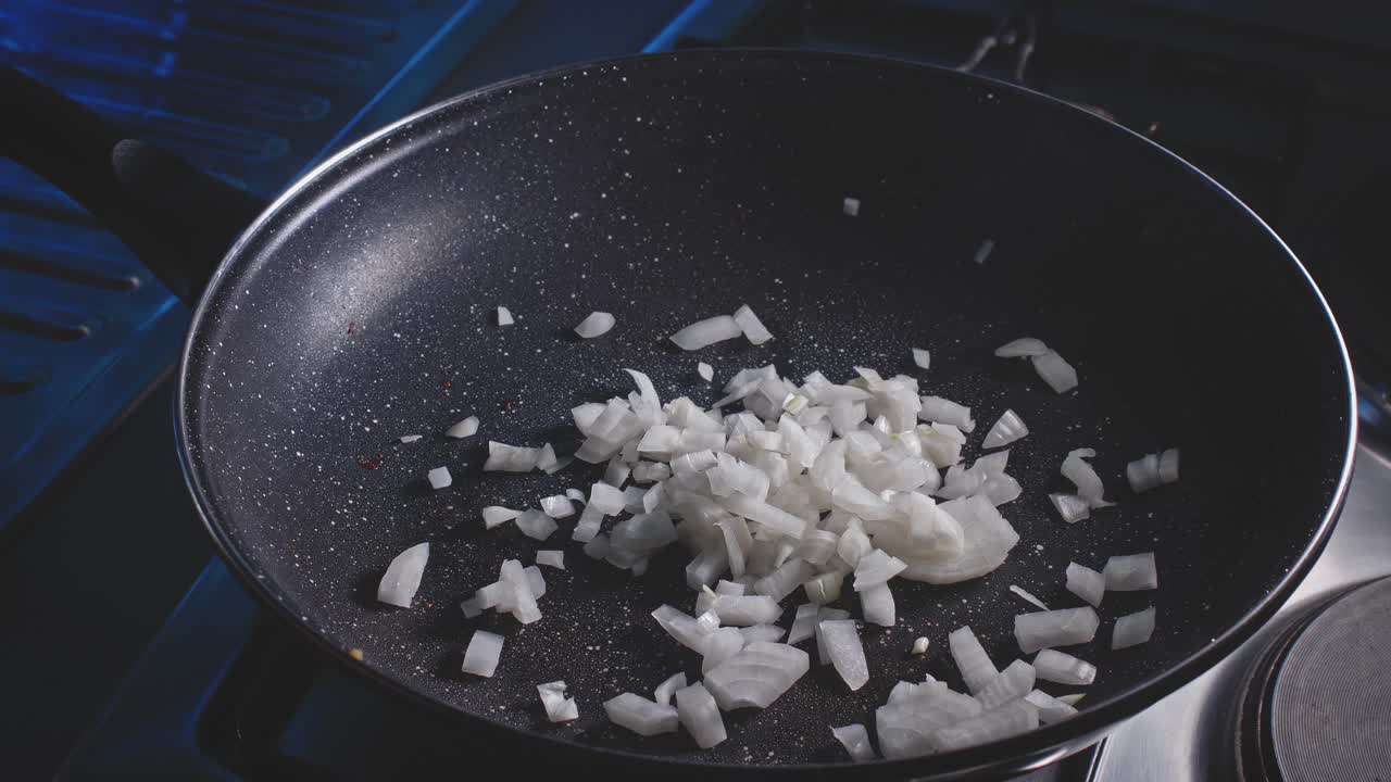 Pouring chopped onion pieces into a frying pan and moving them with a wooden spoon in home kitchen