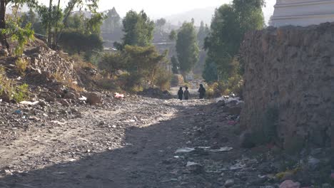 3 children are walking to school in the village with bad and harsh road