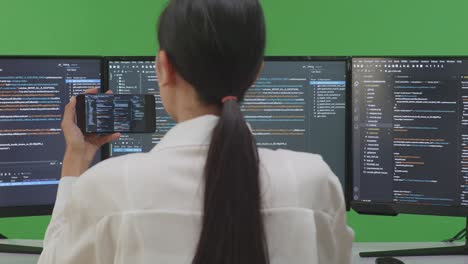 woman programmer coding on multiple monitors and mobile phone