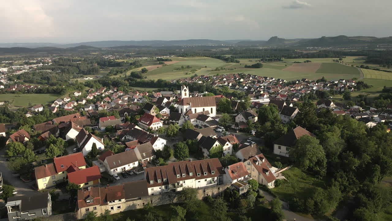 Drone footage revealing the historic hilltop town of Aach in Baden-Württemberg. As the drone ascends, it showcases the charming old town and the surrounding village below.