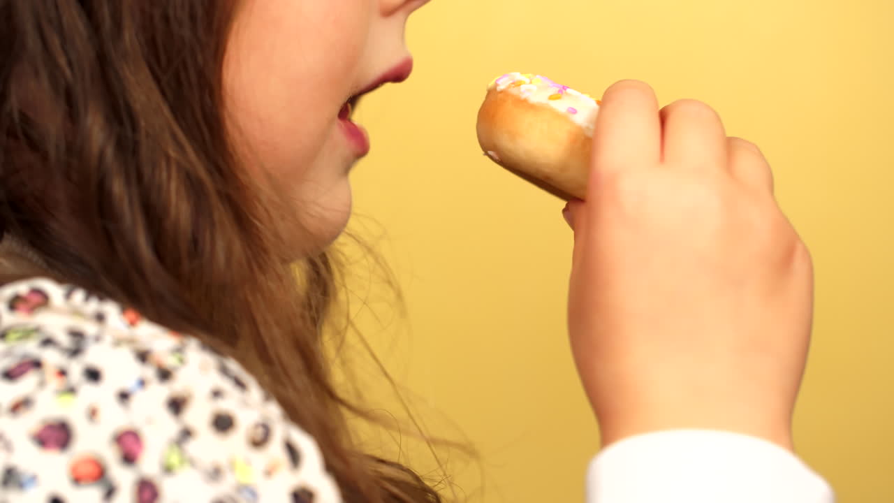 Side Profil of Cute Child eating donut in front of yellow background. Young girl eat doughnut while having fun and doing silly faces.