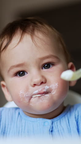 cute kid eating porridge from spoon. mother gives porridge to baby and takes the porridge out of kid's face. vertical video