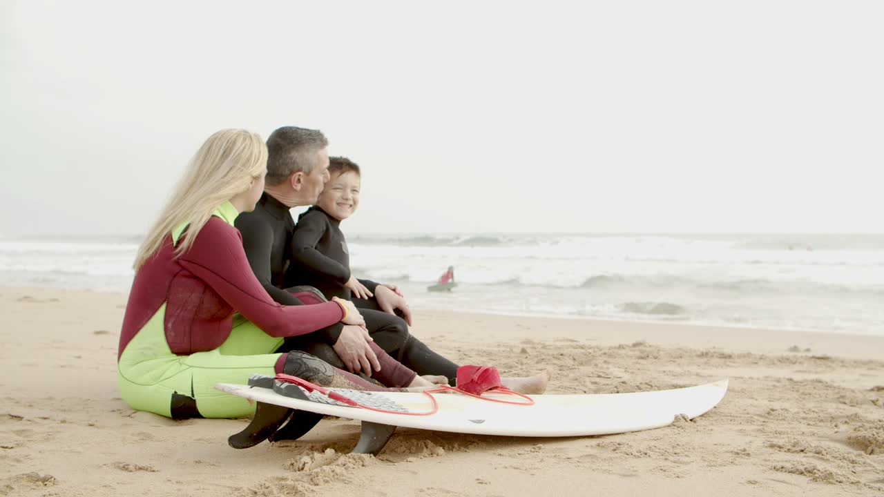 familia feliz en trajes de neopreno sentados en la playa