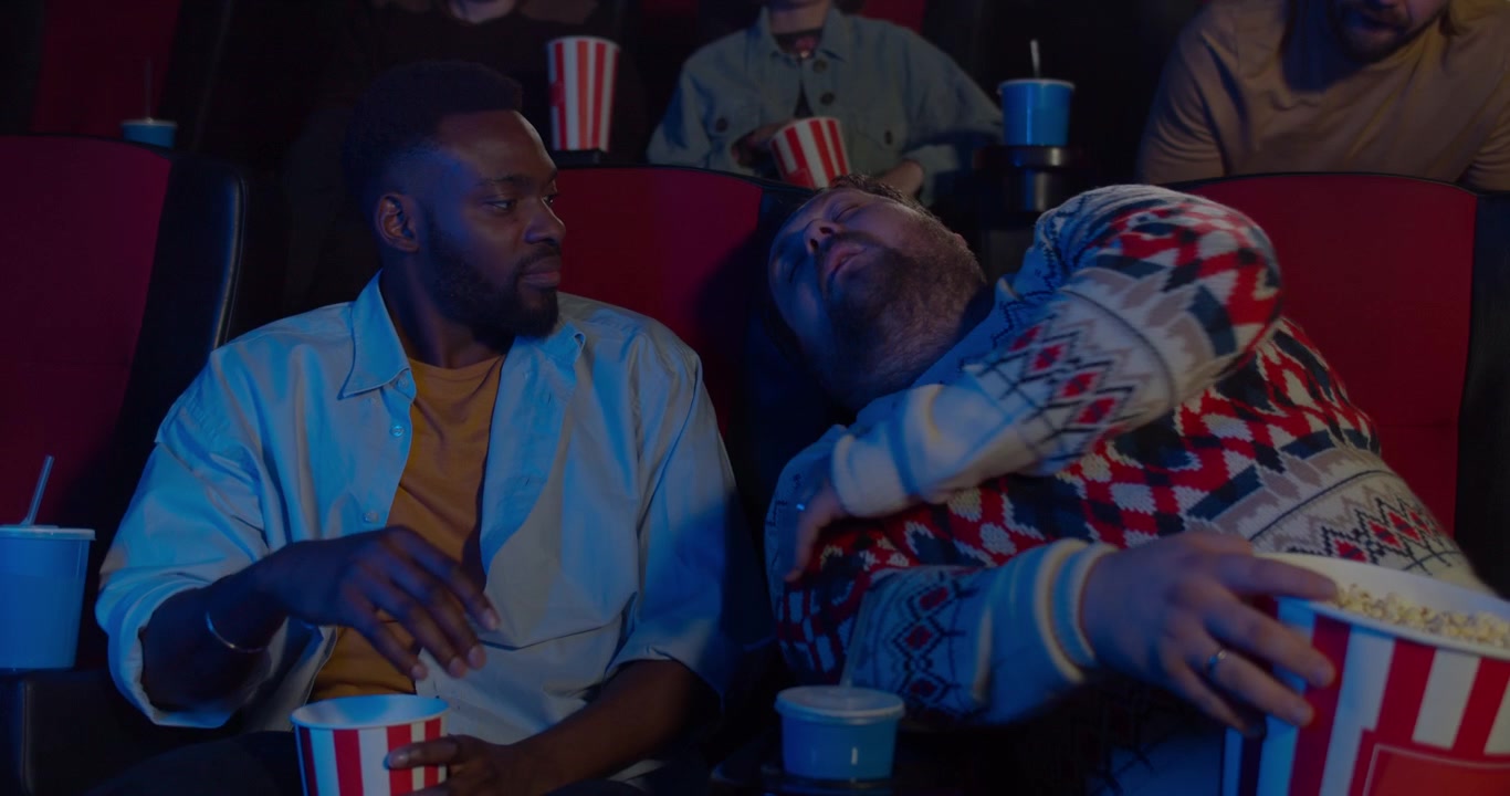 Uomo che dorme al cinema mentre un amico guarda il film.