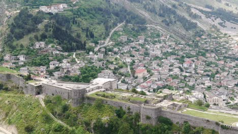 Drone-view-in-Albania-flying-in-Gjirokaster-town-over-a-medieval-castle-on-high-ground-fort-showing-the-brick-brown-roof-houses