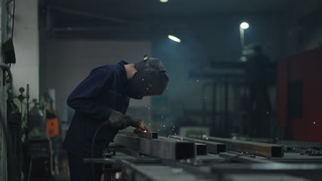 industrial welder with torch. welding mask and welders leathers weld metal with a arc welding machine at the construction site blue sparks fly to the sides