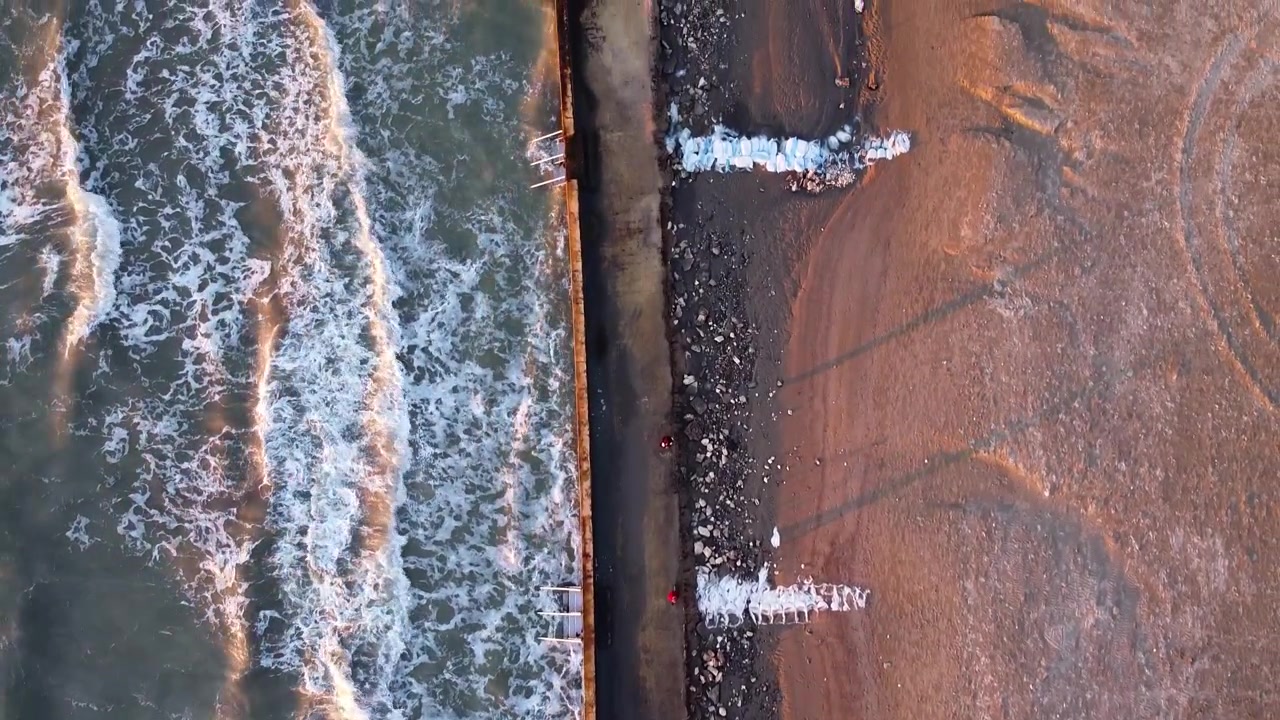 Luftfoto ovenfra av den albanske kystlinjen med bølger som slår mot gangveien på stranden.