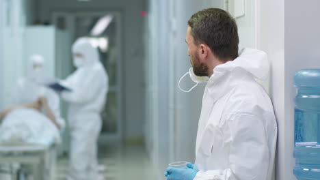 er doctor in protective suit drinking water on break in hospital