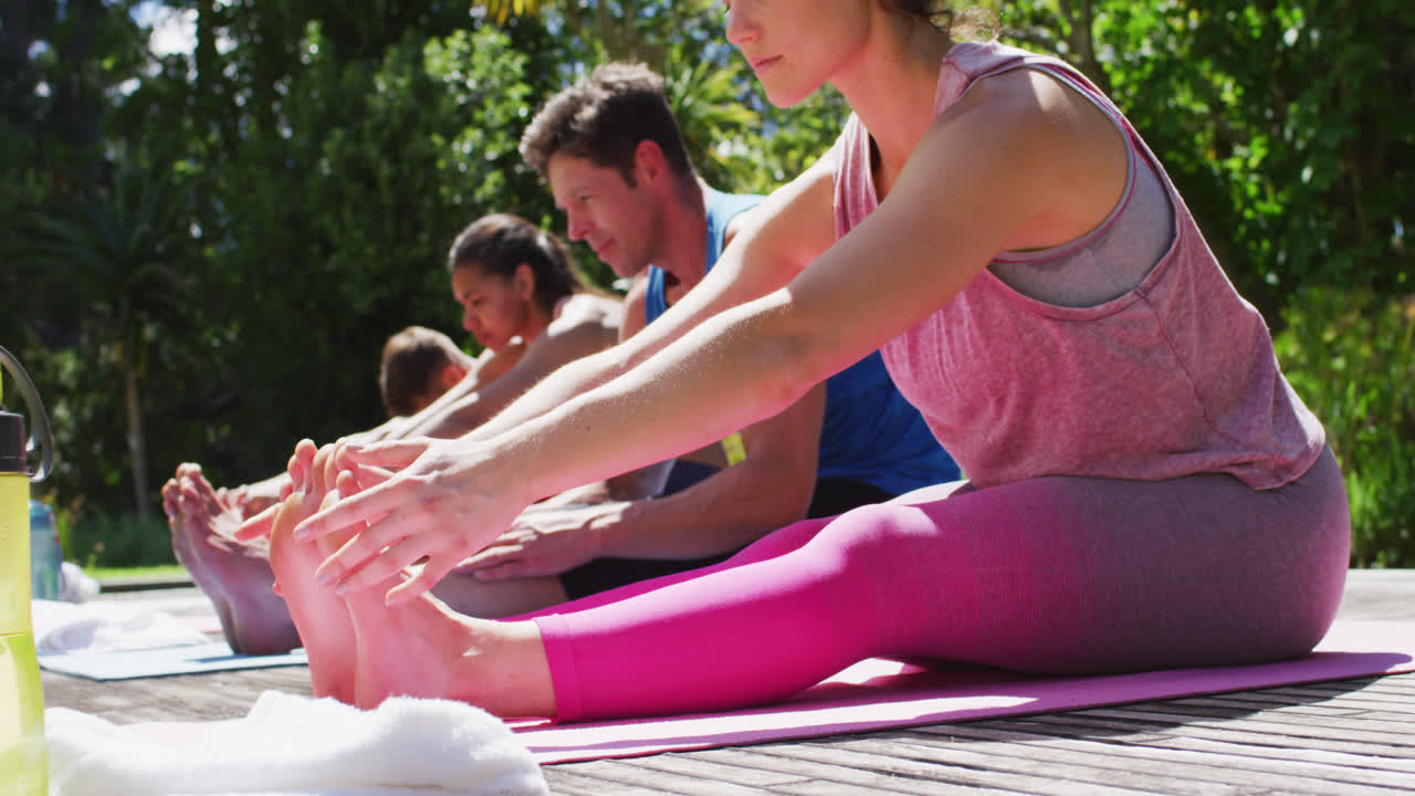 grupo diverso de hombres y mujeres practicando yoga, estiramiento, sentados en esteras en un parque soleado