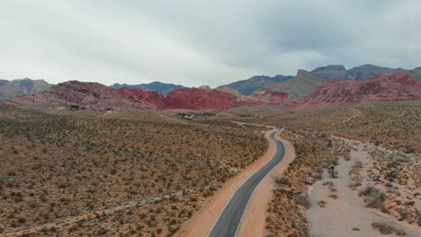 Aerial-drone-shot-of-an-empty-desert-road-with-scenic-mountains-in-the-background