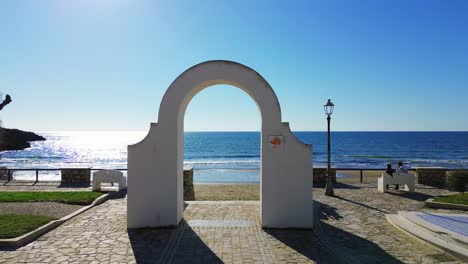 sunlit coastal town of gaeta, lazio, aerial dolly through white arch over sandy beach and ocean water