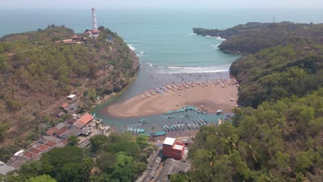 Aerial-view-of-bay-between-cliffy-shoreline-with-fishing-boats-harbor-and-sandy-beach