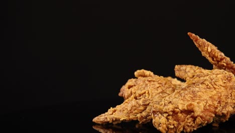 golden fried chicken wings rotate smoothly on a glossy black surface, illuminated by soft studio lighting, highlighting their crunchy texture and appetizing appearance