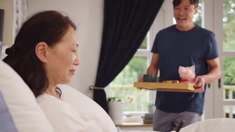 mature asian man bringing wife using mobile phone breakfast in bed to celebrate birthday or anniversary - shot in slow motion