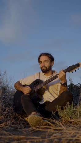 a man playing an acoustic guitar outdoors at sunset or sunrise