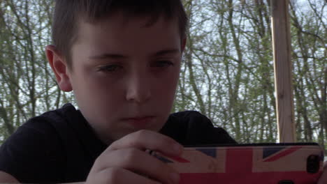 niño sentado afuera, disfrutando de su teléfono inteligente, jugando juegos, cámara lenta