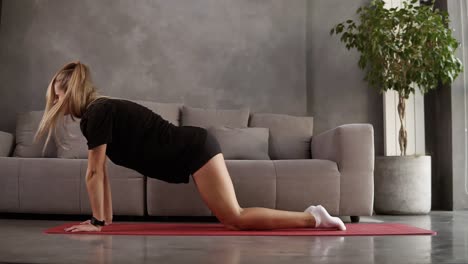 Caucasian-woman-in-black-sport-clothes-doing-morning-sport-exercise-at-home-stretching-on-red-mat.-Flexible-girl-practicing-vinyasa-yoga-surya-namaskar,-stretching-her-body-in-her-living-room.-Healthy-lifestyle-body-care