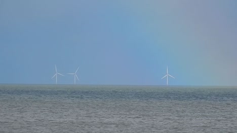 rainbow alongside offshore green energy wind turbine farm seascape