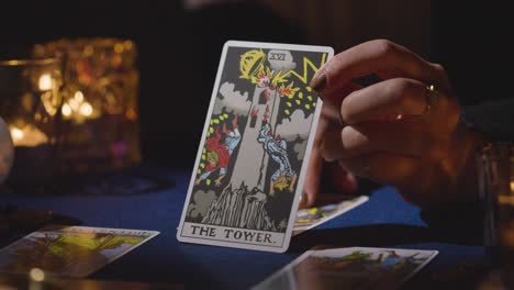 close up of woman giving tarot card reading on candlelit table holding the tower card 5