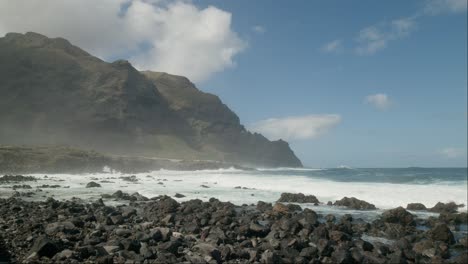 view of black stones, rocky volcanic beach, mountains coastline, and the atlantic ocean