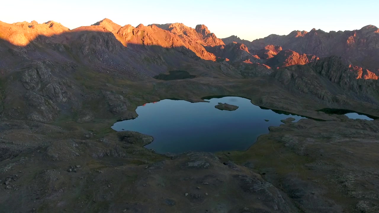 Luftfoto af alpinsø omgivet af barske bjerge ved solnedgang