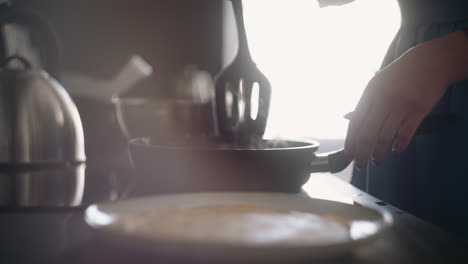 woman is cooking homemade food frying pancakes in sunday morning closeup of stove with frying pan
