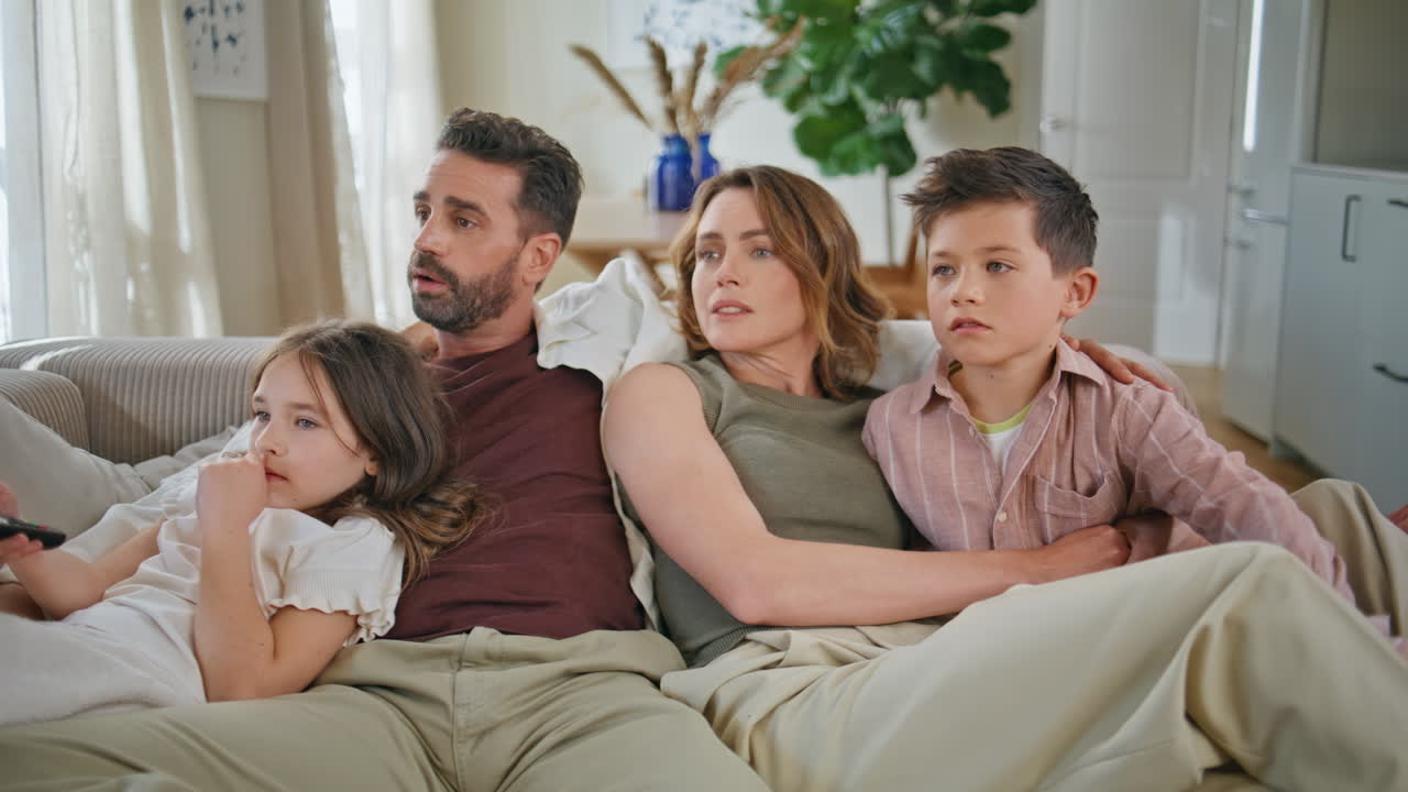 Primer plano de una familia acurrucada en el sofá. Padres e hijos felices viendo una película de forma divertida