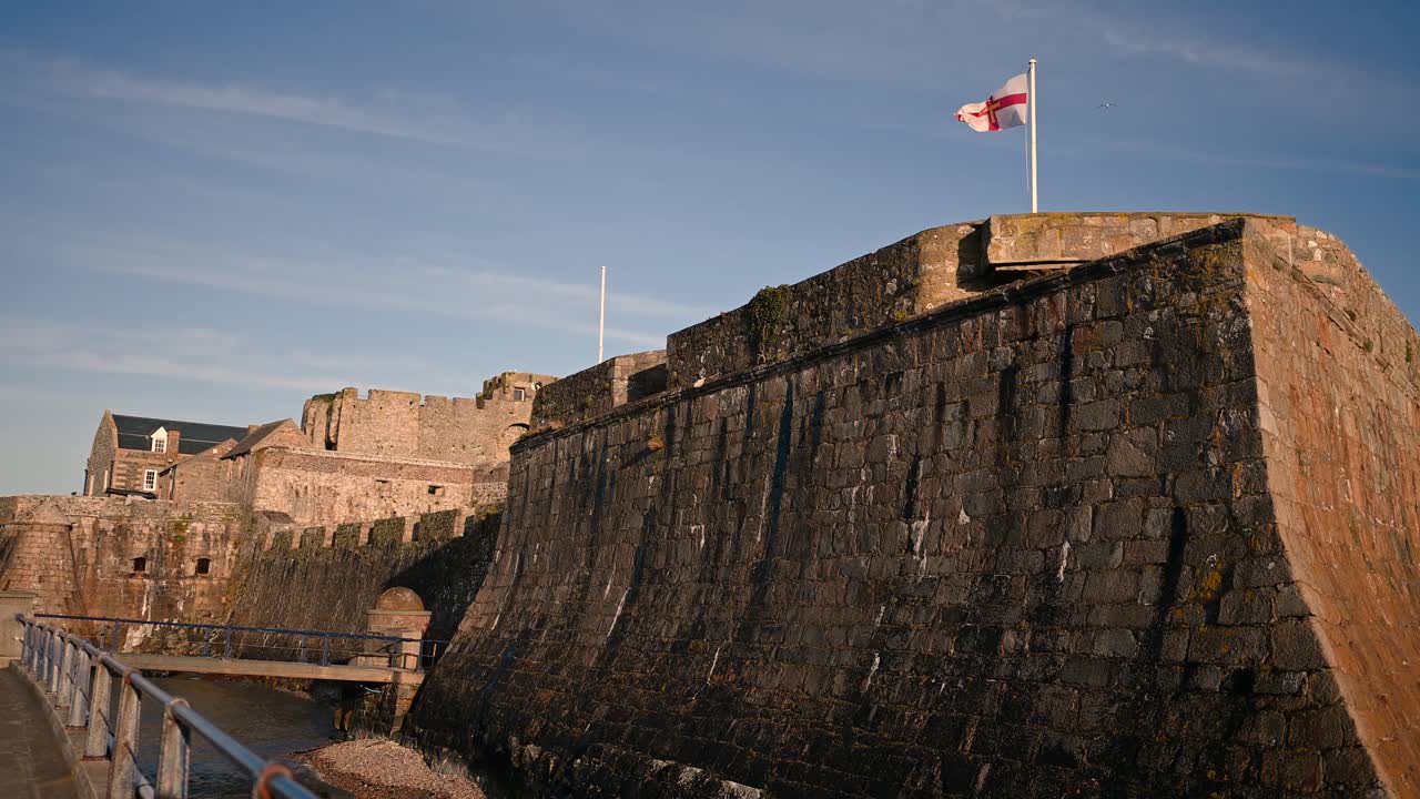 la bandera de guernsey ondeando desde las almenas del castillo cornet st. peter port en una fuerte brisa con cielos azules en un día soleado con plena perspectiva del castillo