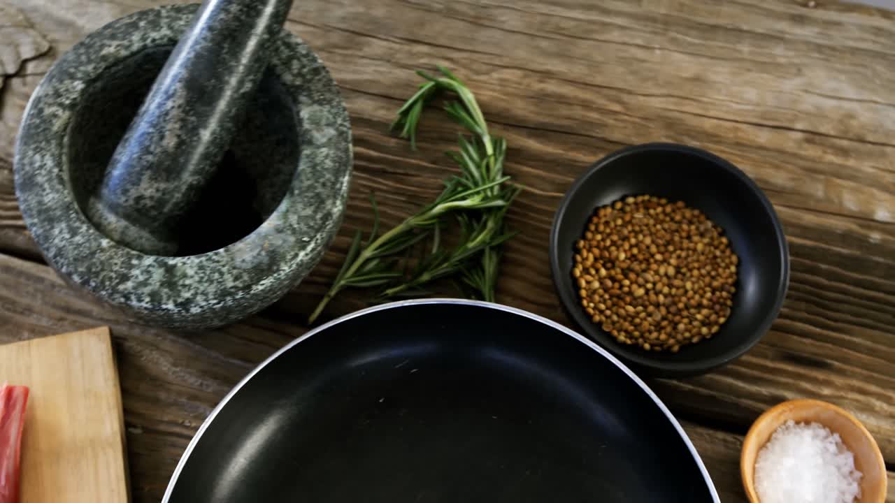 bistec crudo, ingredientes y sartén en una mesa de madera