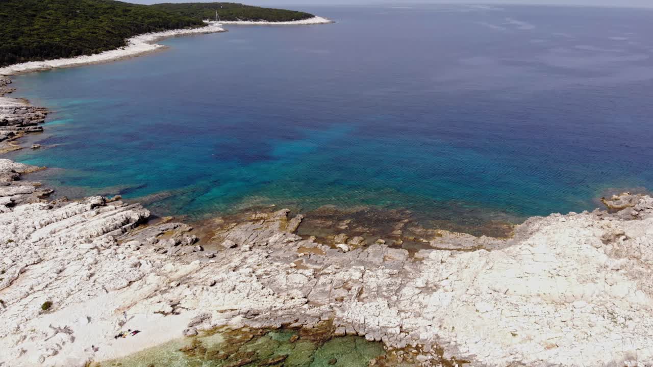 un banco de arena rocoso que divide las claras aguas azules de la playa de paralia emplisi con pequeñas olas ondeando en la superficie en erisos, grecia - toma aérea en movimiento hacia adelante
