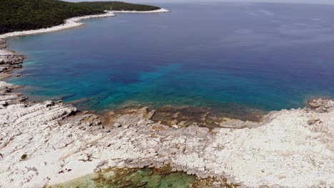 a rocky sandbar dividing the clear blue seawaters of paralia emplisi beach with small waves rippling on the surface in erisos, greece - forward moving aerial shot