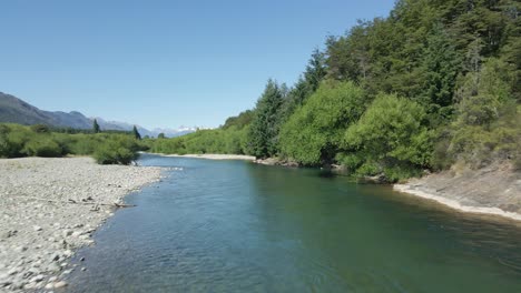 Aerial-dolly-in-of-Rio-Azul-stream-flying-under-elevated-bridge-between-trees-and-mountains,-Patagonia-Argentina