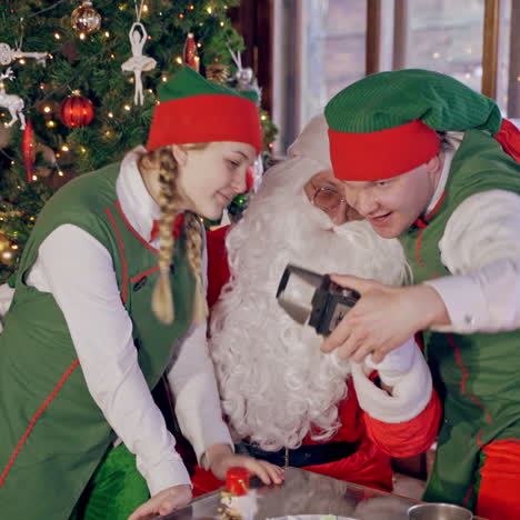 santa with elves doing selfie. joyful santa together with fairy characters making photo on christmas background indoors. new year holidays.