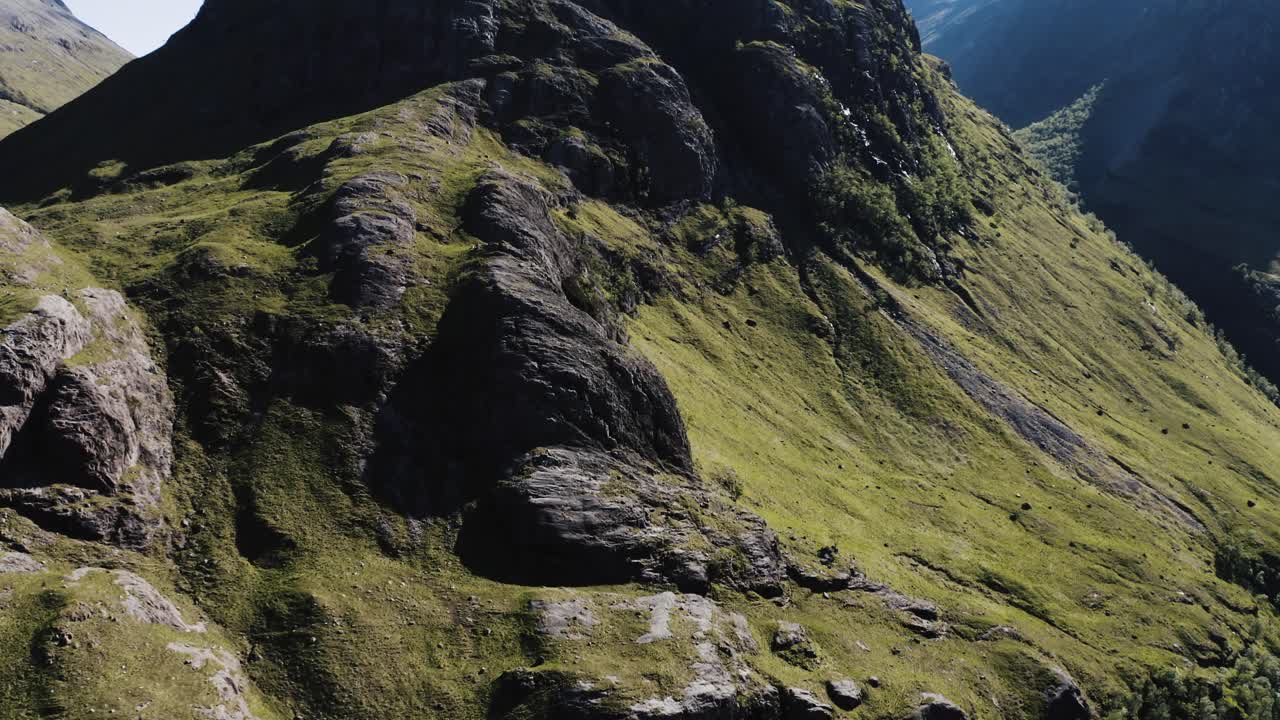 un avión no tripulado se inclina hacia arriba para revelar un alto pico en el valle de glencoe, escocia