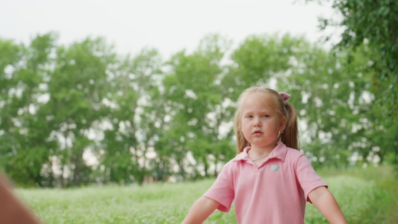 Joven blanca curiosa cerca de una manta colocada en un prado rural, examinando la tela sostenida por un compañero invisible, expresión pensativa, pantalones cortos vaqueros y coletas, suave anticipación a la luz natural
