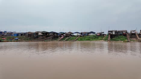 wide view of traditional stilt houses lined along the edge riverbank of cambodia