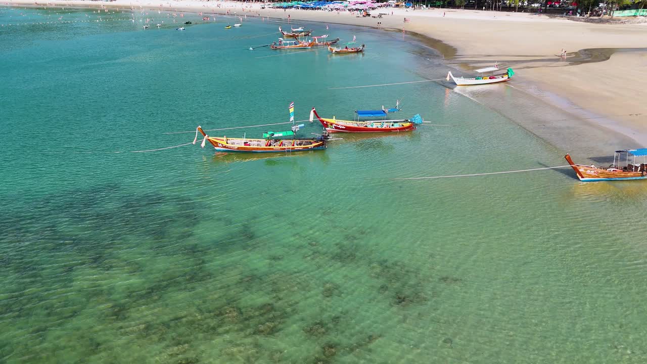 las imágenes de drones capturan vibrantes barcos de cola larga navegando por las aguas claras de phuket, tailandia, mostrando una escena de playa bulliciosa