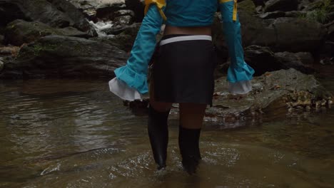 la cosplayer camina en el agua en la base de una cascada y revela su disfraz de lucy hearfilia.