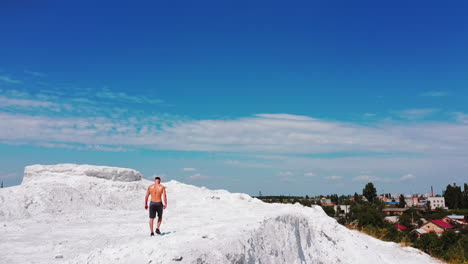 back view of a sportsman without shirt in canyon on the city background. athlete in shorts walking on white hill under blue sky in a sunny summer day.