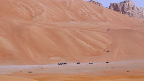 grupo de vehículos golpeando dunas en dunas elevadas del desierto cerca de roca fósil en sharjah, emiratos árabes unidos