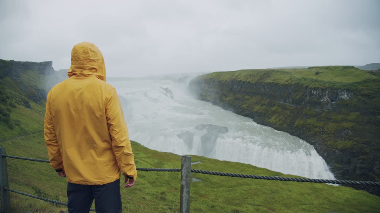 turista masculino con impermeable amarillo en la cascada de gullfoss en islandia en la naturaleza islandesa.